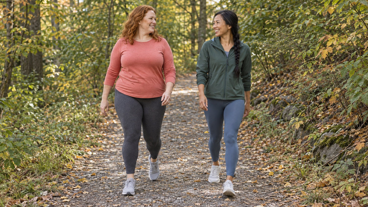 Two women share an easy conversational-pace walk on a tree-lined trail
