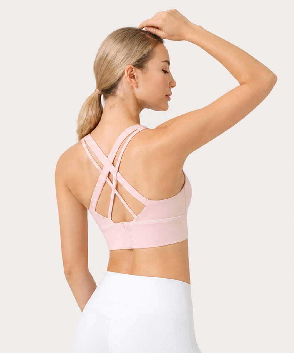 Back view of a woman wearing a pale pink cross-strap sports bra and white bottoms